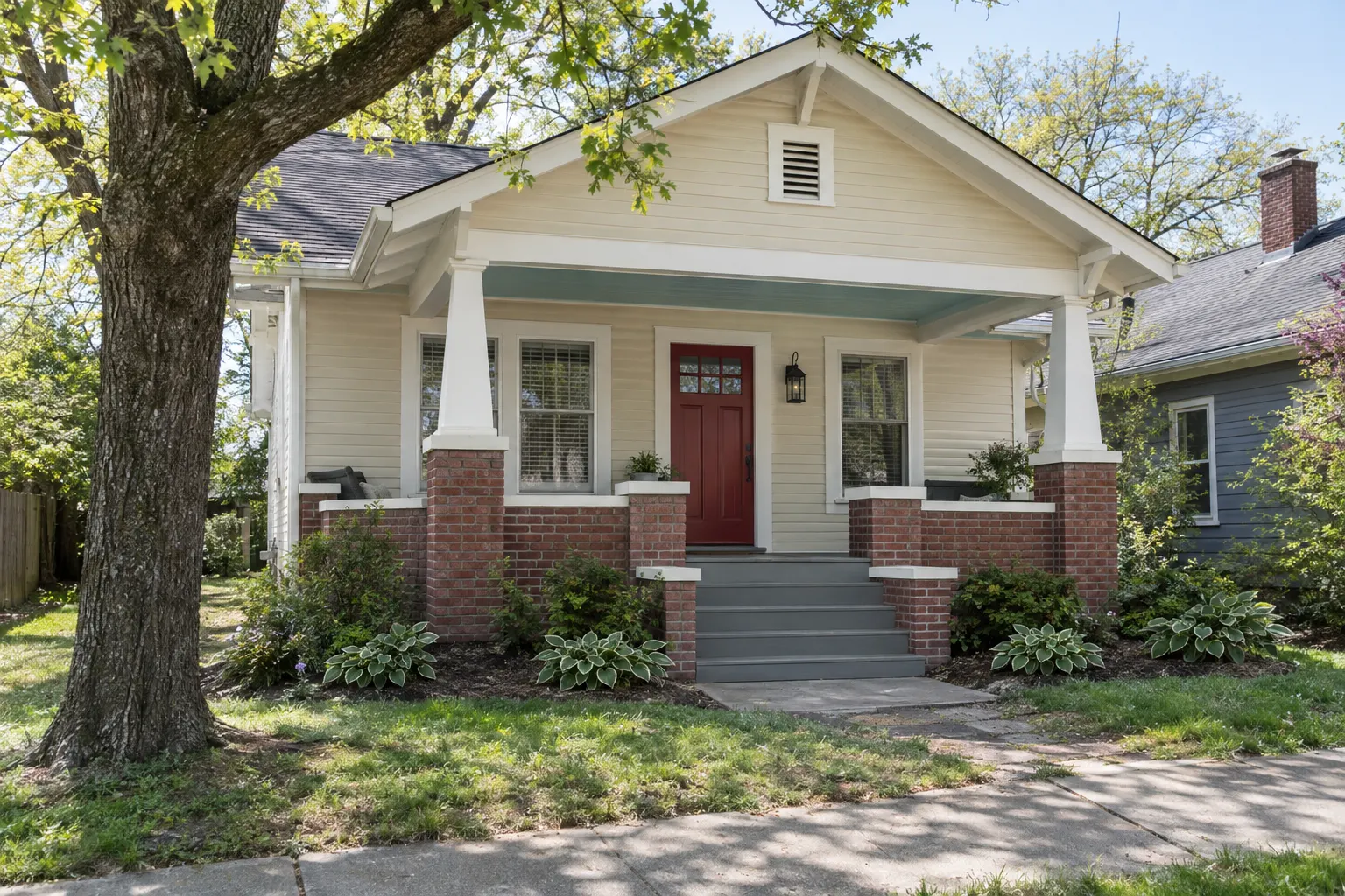 Example image, not one of our jobs: a freshly painted craftsman bungalow with cream siding, white trim and columns on brick piers, a pale blue porch ceiling and a brick-red front door.